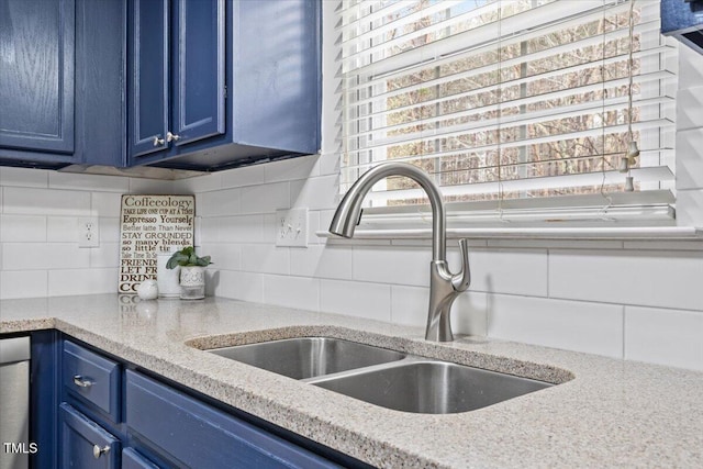 interior details with blue cabinets, light stone counters, decorative backsplash, and a sink