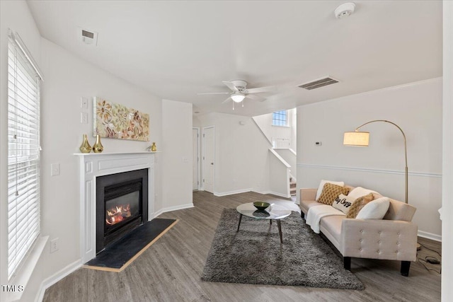 living area with a glass covered fireplace, wood finished floors, visible vents, and stairs