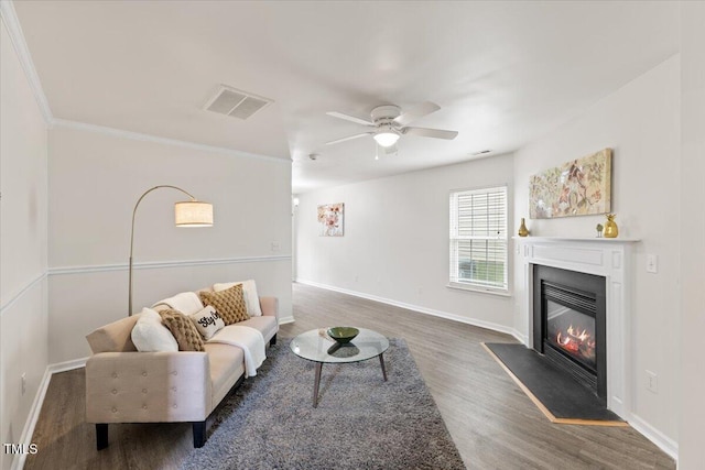 living area with a glass covered fireplace, wood finished floors, visible vents, and baseboards