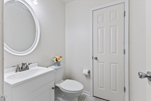 half bathroom with toilet, baseboards, and vanity