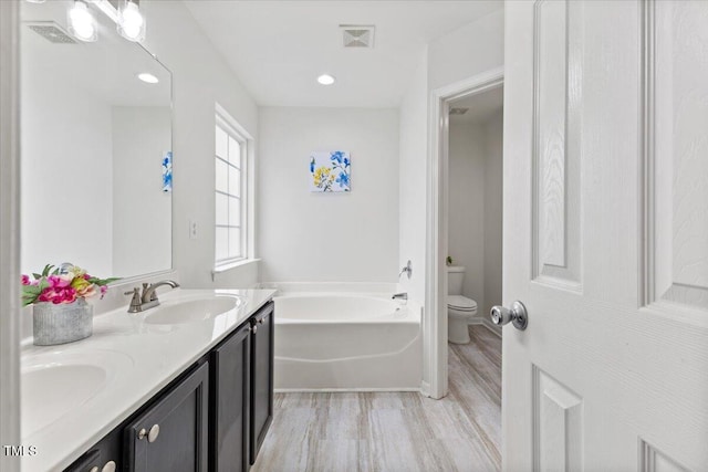 bathroom featuring double vanity, visible vents, toilet, a sink, and a bath