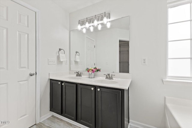 full bathroom with double vanity, a sink, a tub, and baseboards