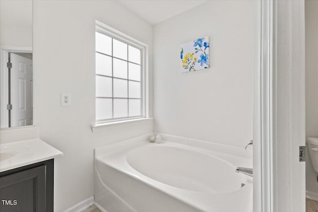 bathroom with toilet, a garden tub, and vanity