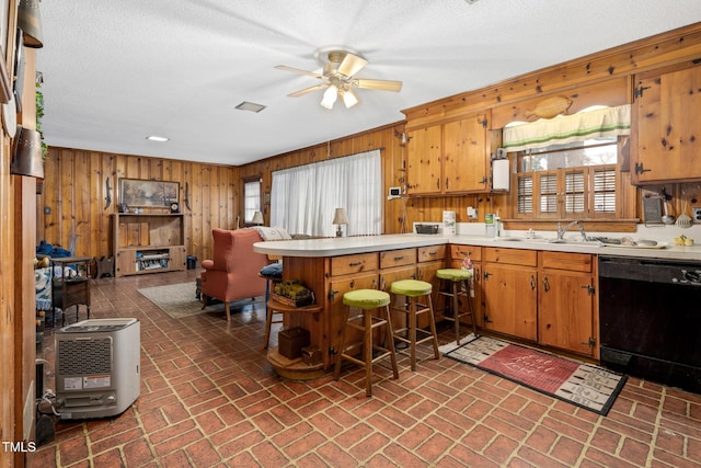 kitchen featuring ceiling fan, dishwasher, kitchen peninsula, wood walls, and a textured ceiling