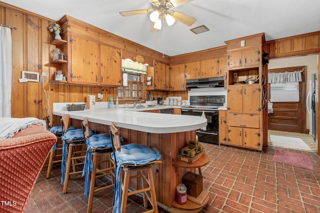 kitchen with kitchen peninsula, a textured ceiling, black range with electric cooktop, wooden walls, and sink