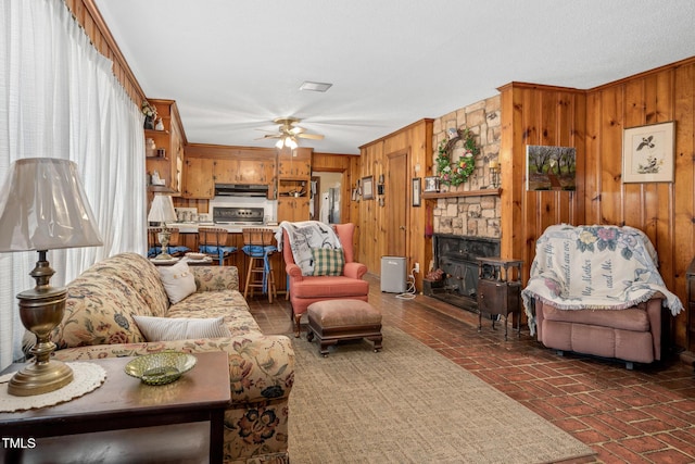 living room featuring a fireplace, ornamental molding, ceiling fan, and wooden walls