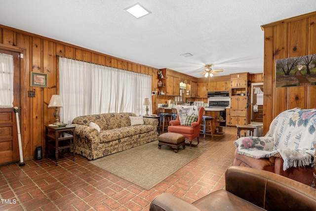 living room featuring wooden walls, ceiling fan, a healthy amount of sunlight, and a textured ceiling