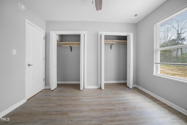 unfurnished bedroom featuring light hardwood / wood-style flooring, multiple windows, and multiple closets