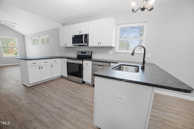 kitchen featuring kitchen peninsula, stainless steel appliances, vaulted ceiling, sink, and decorative light fixtures