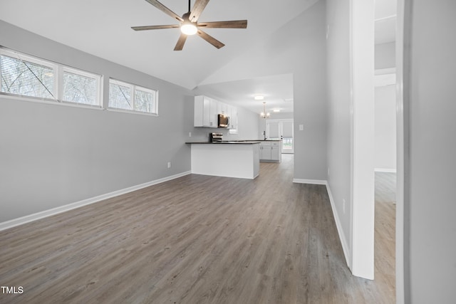 unfurnished living room with light hardwood / wood-style flooring, high vaulted ceiling, and ceiling fan with notable chandelier