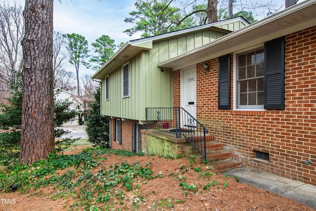 entrance to property featuring board and batten siding, crawl space, and brick siding