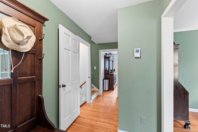 hallway with stairs, light wood finished floors, and baseboards