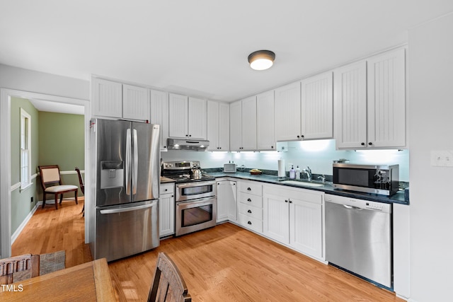 kitchen with light wood-style floors, dark countertops, appliances with stainless steel finishes, under cabinet range hood, and a sink