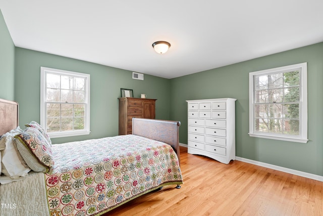 bedroom with baseboards, multiple windows, visible vents, and wood finished floors