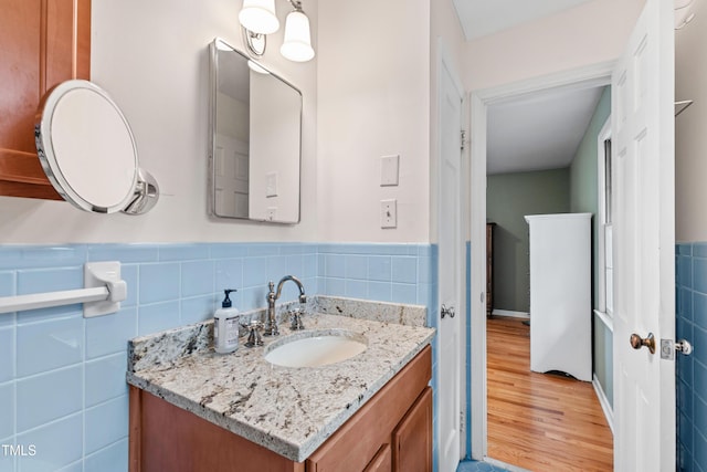 bathroom featuring wood finished floors, wainscoting, vanity, and tile walls