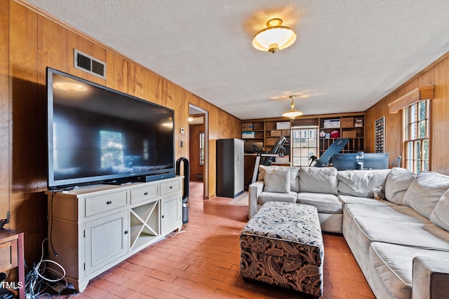 living area with brick floor, visible vents, wood walls, and a textured ceiling