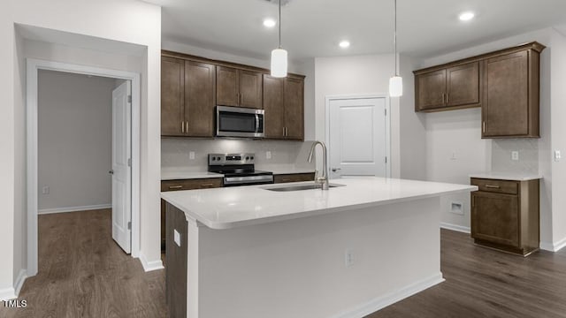 kitchen featuring decorative light fixtures, sink, stainless steel appliances, and a kitchen island with sink