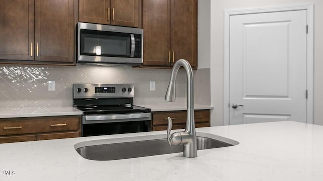 kitchen with light stone countertops, appliances with stainless steel finishes, dark brown cabinetry, and tasteful backsplash