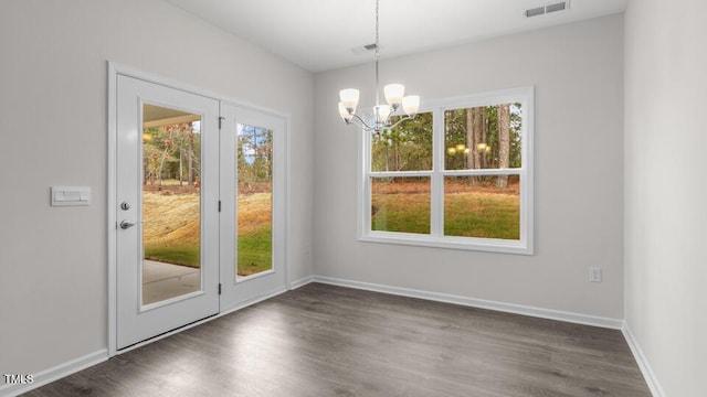 unfurnished dining area with plenty of natural light, dark wood-type flooring, and a notable chandelier