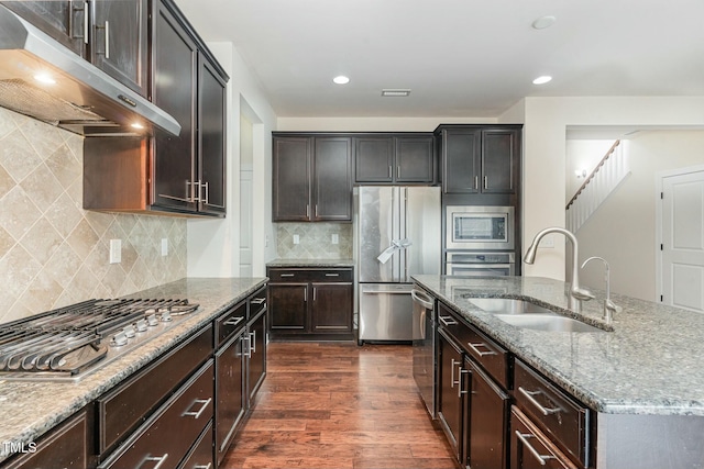 kitchen with sink, stainless steel appliances, light stone counters, a center island with sink, and dark hardwood / wood-style flooring