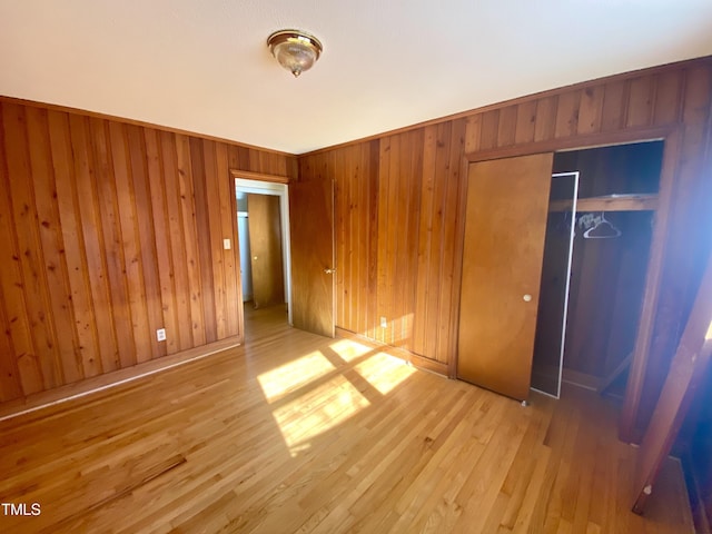 unfurnished bedroom with light wood-type flooring, a closet, and wooden walls