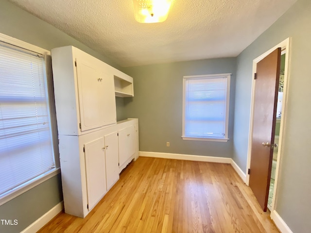 kitchen with light wood-type flooring, white cabinetry, and a textured ceiling