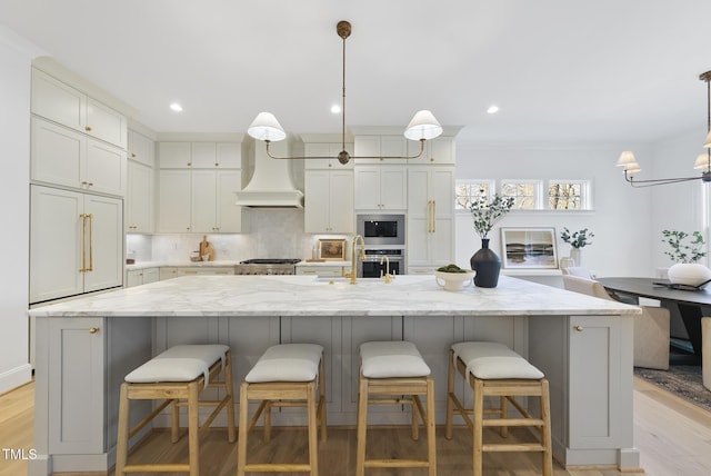 kitchen with light stone counters, hanging light fixtures, a spacious island, and light hardwood / wood-style floors