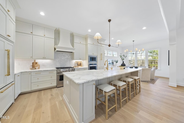 kitchen with a large island, light hardwood / wood-style flooring, premium range hood, built in appliances, and a kitchen bar