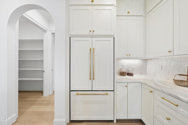 kitchen with decorative backsplash, light stone counters, paneled fridge, light hardwood / wood-style floors, and white cabinetry