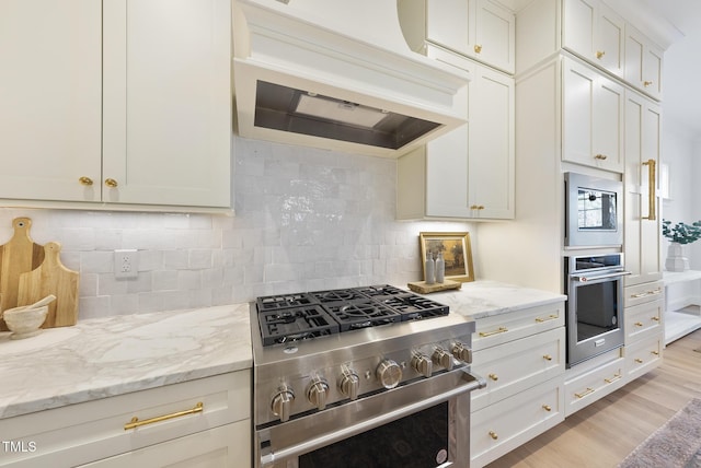 kitchen with decorative backsplash, light wood-type flooring, appliances with stainless steel finishes, light stone counters, and custom range hood