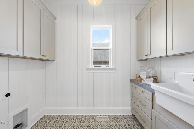 laundry area featuring electric dryer hookup, wood walls, sink, and cabinets