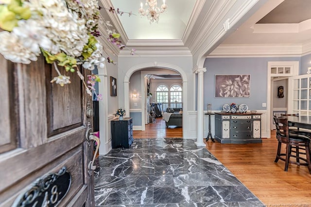 foyer entrance with a chandelier, crown molding, a wainscoted wall, decorative columns, and arched walkways