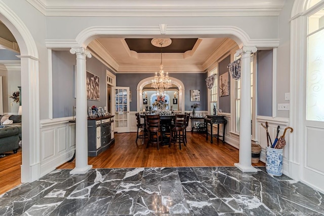 dining space featuring ornamental molding, ornate columns, a raised ceiling, arched walkways, and wood finished floors
