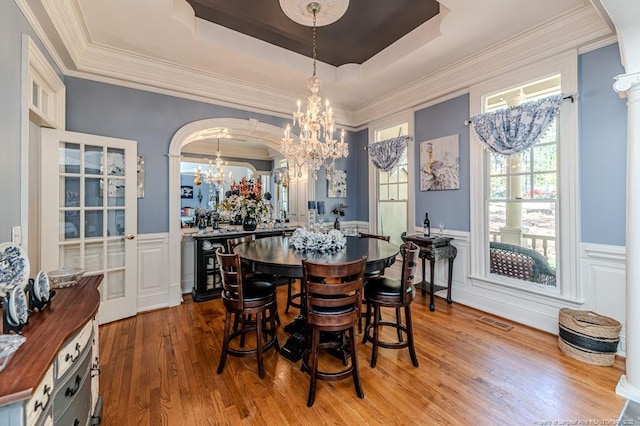 dining room with a chandelier, a wainscoted wall, visible vents, a raised ceiling, and wood finished floors