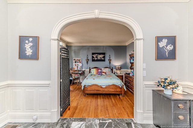 bedroom featuring crown molding, arched walkways, wainscoting, and wood finished floors