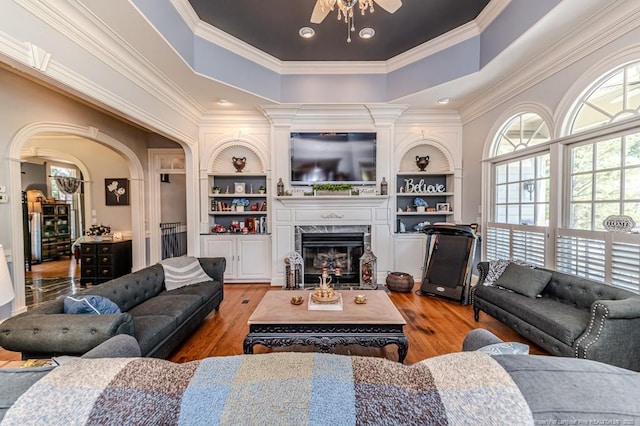 living area featuring light wood-type flooring, crown molding, a fireplace, and a ceiling fan