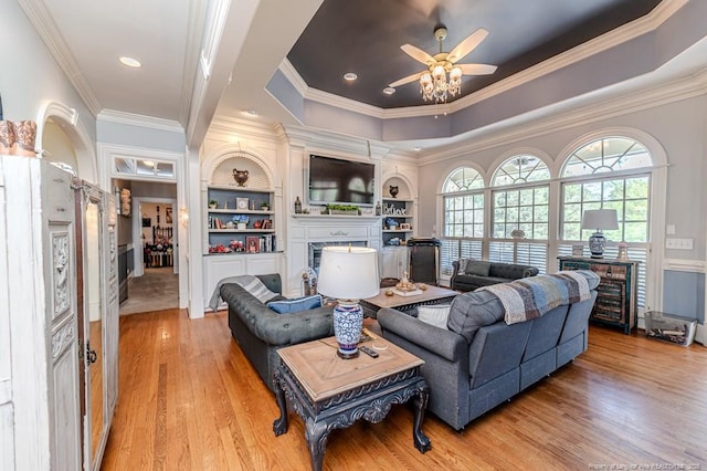 living room with ornamental molding, a ceiling fan, light wood-style floors, a fireplace, and a tray ceiling
