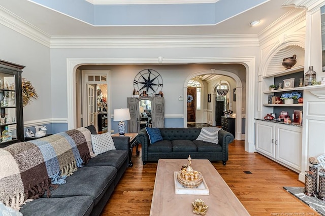 living room featuring arched walkways, wood finished floors, and ornamental molding