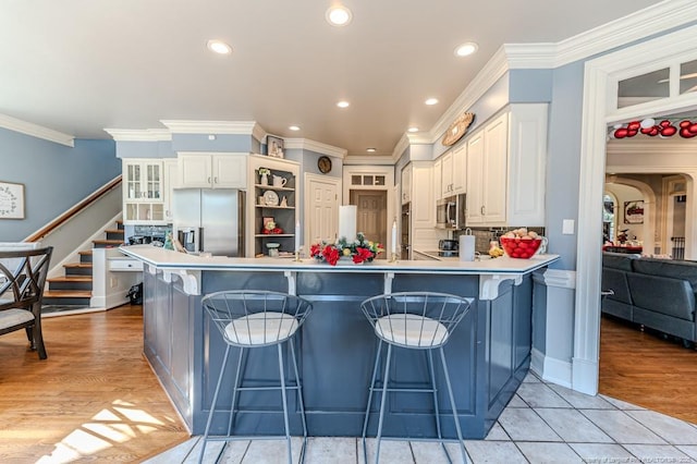 kitchen featuring a peninsula, crown molding, white cabinets, a kitchen bar, and stainless steel appliances