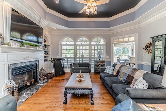 living area featuring a premium fireplace, crown molding, wood finished floors, and a ceiling fan