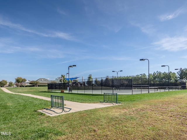 view of home's community featuring a tennis court, a lawn, and fence