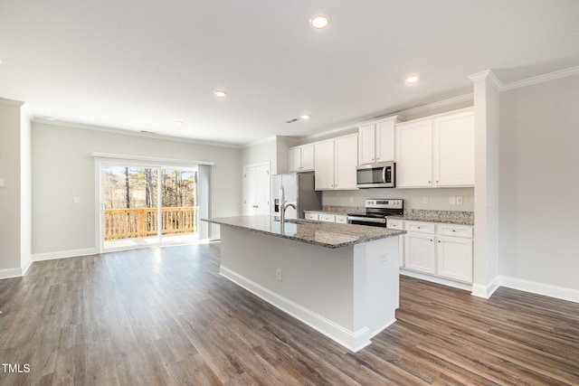 kitchen with white cabinets, appliances with stainless steel finishes, dark stone counters, an island with sink, and ornamental molding