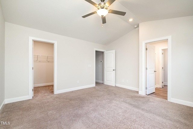 unfurnished bedroom featuring a spacious closet, a closet, vaulted ceiling, ceiling fan, and light colored carpet