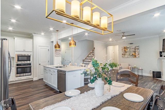 kitchen featuring stainless steel appliances, sink, decorative light fixtures, white cabinetry, and an island with sink