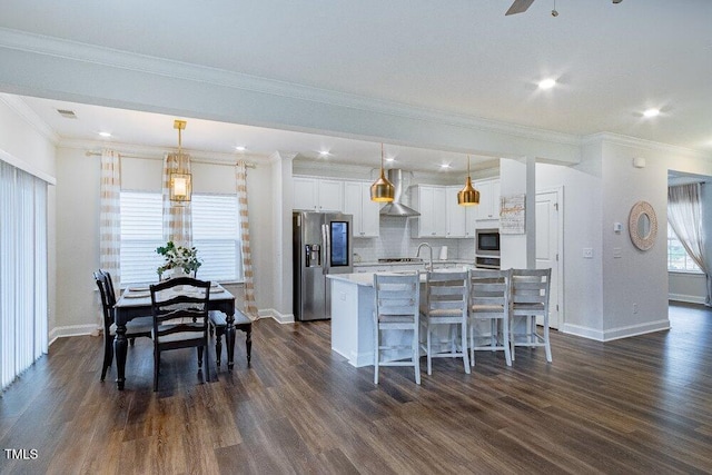 kitchen featuring dark wood-type flooring, pendant lighting, stainless steel appliances, and wall chimney exhaust hood