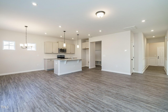 kitchen with appliances with stainless steel finishes, decorative light fixtures, dark hardwood / wood-style floors, white cabinetry, and an island with sink