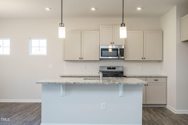 kitchen with light stone countertops, appliances with stainless steel finishes, pendant lighting, and an island with sink