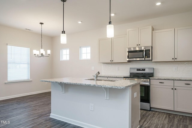 kitchen with light stone countertops, sink, stainless steel appliances, a kitchen island with sink, and white cabinets