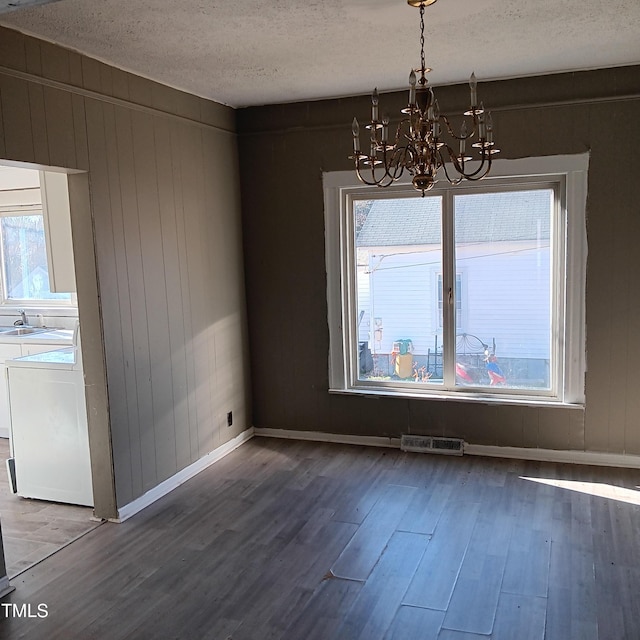 unfurnished dining area with a chandelier, a textured ceiling, dark hardwood / wood-style floors, and a healthy amount of sunlight