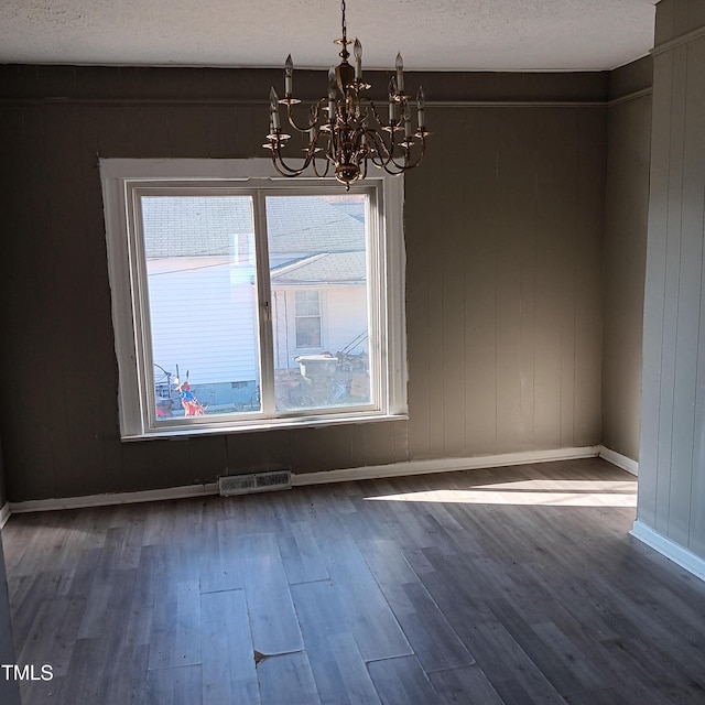 unfurnished dining area with hardwood / wood-style floors, a textured ceiling, and an inviting chandelier